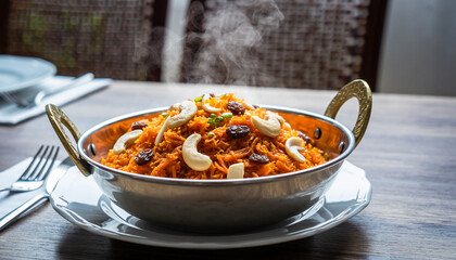 This ultra-high-resolution food image features authentic Indian gajar halwa served hot in a traditional stainless steel bowl, photographed at a visually appealing 45-degree angle. The rich carrot text