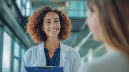 A female doctor in a white coat speaks with a patient in a modern hospital corridor showing a calm professional medical setting.