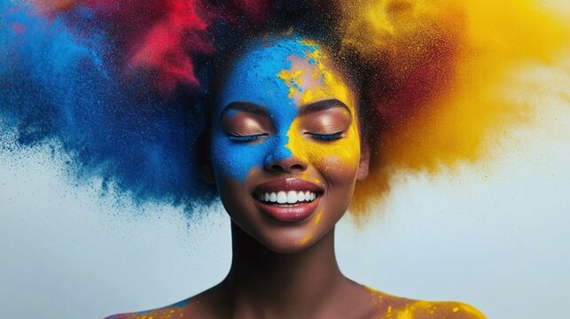 Smiling woman with closed eyes covered in vibrant blue and yellow powder with colorful red, blue, and yellow powder exploding around her head expressing joy and energy