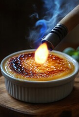 A dessert being caramelized with a flame torch producing smoke and a glowing flame on a wooden surface