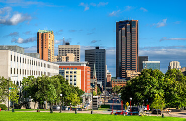 Downtown Saint Paul skyline rises beyond the green lawns of the Minnesota State Capitol Mall. View features Wells Fargo Place and government buildings under a blue summer sky