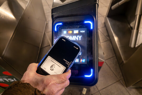 New York, NY USA A hand holds a cell phone to pay for the subway at a turnstile.