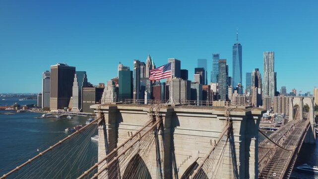 Iconic view of the Brooklyn Bridge with an American flag flying above the granite towers and cables, set against the towering skyscrapers of the Manhattan financial district