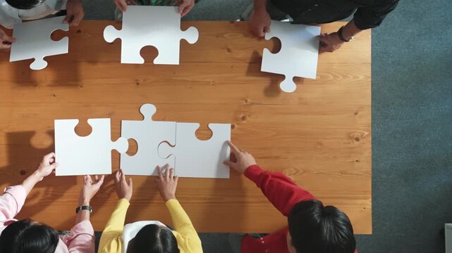 Top down view of skilled business people assemble jigsaw puzzle on meeting table. Group of diverse team working together to solve the puzzle. Represented unity, togetherness, cooperative. Convocation.