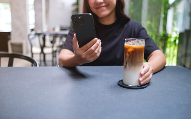 Closeup image of a woman holding and using mobile phone while drinking coffee in cafe