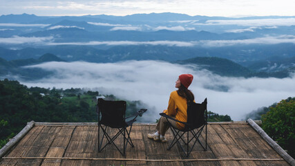 Portrait image of a woman sitting and looking at a beautiful foggy mountain before sunrise