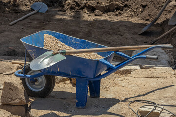 A single-wheeled metal trolley for transporting various materials on a construction site. Construction equipment. Manual labor during restoration work. A shovel on a cart.