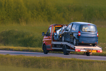 Yellow truck towing damaged car from roadside