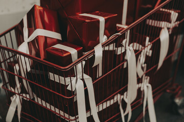 A red shopping cart is overflowing with glossy red gift boxes, tied with elegant white ribbons, the...