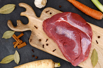top view of raw venison haunch on wooden board with spices and vegetables, ingredients for a delicious roast venison