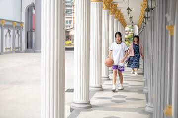 A person teaching basketball techniques to a younger player near building pillars.