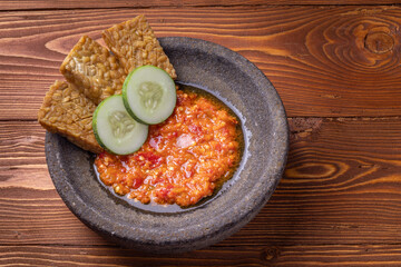 sambal or traditional chili sauce from Indonesia, freshly made using a stone mortar and pestle with fried tempeh and cucumber