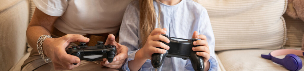 Unrecognizable mother and daughter enjoying leisure time together, playing video games on a console with copy space