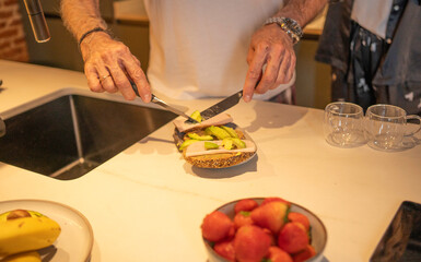 Person making a nutritious open-faced sandwich with avocado and ham in the kitchen