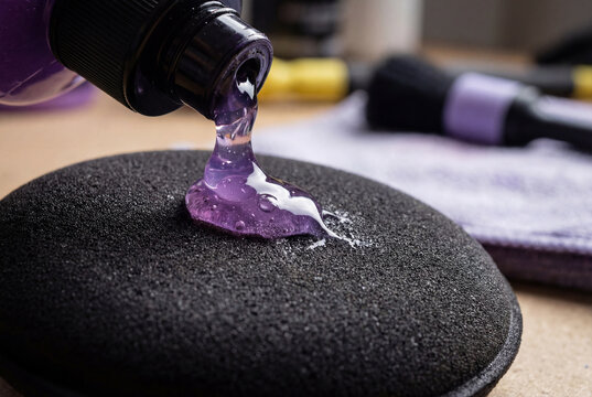 Auto detailing supplies. Pouring purple polishing compound onto a black foam buffing pad. Preparation for car paint correction