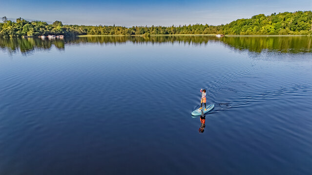 Active woman paddling SUP board on beautiful Lough Key lake, green islands and forest summer landscape on background, stand up paddling water adventure outdoors, Ireland