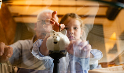 Granddaughter placing coin in a piggy bank with grandfather, learning about savings