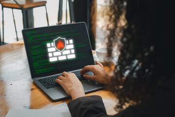 A person working on a laptop displaying a digital firewall icon, symbolizing cybersecurity and data protection.