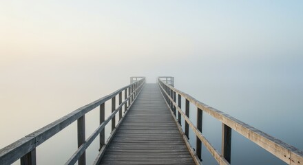 Fototapeta premium A wooden pier extends into a hazy, pale-toned morning mist over a still lake