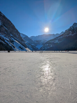 Visitors ice skate on a natural ice rink - frozen Lake Louise in winter. Winter landscape in snow-capped mountains passes by a frozen lake leading to the town - Lake Louise, Alberta, Canada.