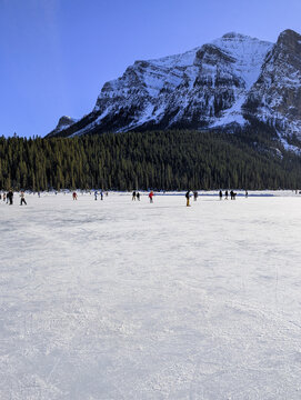 Visitors ice skate on a natural ice rink - frozen Lake Louise in winter. Winter landscape in snow-capped mountains passes by a frozen lake leading to the town - Lake Louise, Alberta, Canada.