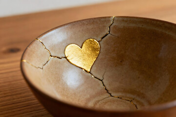 Cracked ceramic bowl repaired with a golden heart, symbolizing beauty in imperfections
