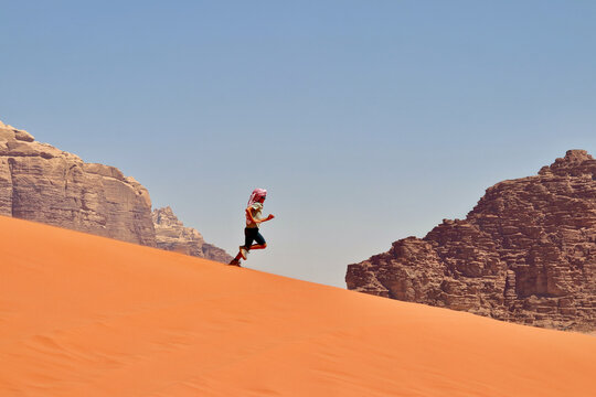 Small six years old kid enjoying his time playing and running down a beautiful dune at Wadi Rum desert, one of the most amazing spots in Jordan.