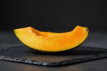 Ripe mango slice with glossy bright orange flesh set on dark slate background