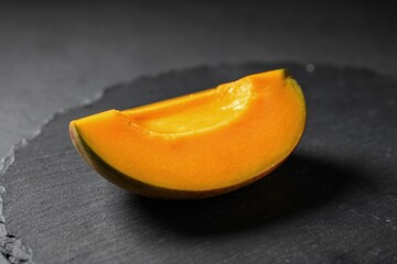 Single ripe mango slice with vivid orange flesh on dark slate surface, glossy