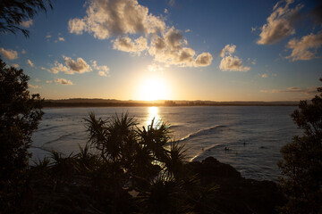 An idyllic view of The Pass, a world renowned surf beach located in Byron Bay in New South Wales, Australia. Captured looking out towards a golden setting sun from the Pass Lookout on dusk.