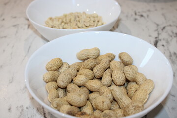 Bowls of raw and shelled peanuts on a marble table during a snack preparation event