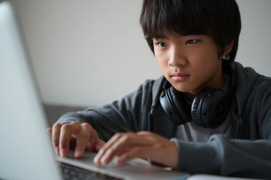 Focused teenage boy with short dark hair using laptop and headphones, studying - Powered by Adobe