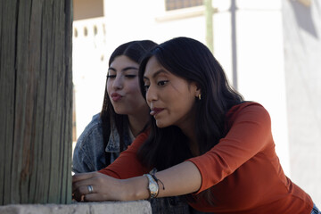 Obraz premium Close-up of young women taking selfies with their cell phones, making funny faces outdoors, showing friendship, joy and carefree youth in an urban environment.