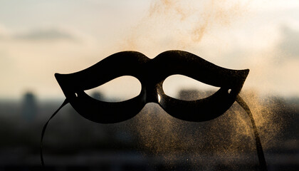 Black masquerade mask with mustache shape against a blurred golden hour city background with shimmering dust.