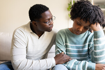 Man comforting sad girlfriend at home on the sofa