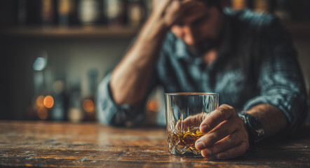 Depressed young man holding a glass of whiskey at a table symbolizing alcoholism stress and addiction
