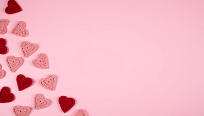 Handmade crochet hearts scattered on a soft pink background for Valentine's Day