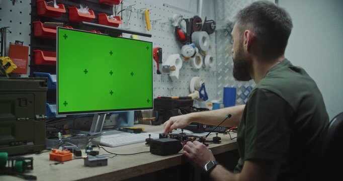 Engineer Building Drone With Dedicated Computer Display. Focused Man Working in Technical Workshop. Man Building Drone With Unedited Green Screen Monitor Used For Displaying Schematics or Software.