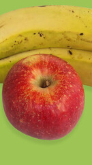 Red apple placed in front of ripe yellow bananas on a vibrant green background