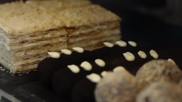 Assortment of layered flaky cake slices, chocolate eclairs with cream dots, and crumb-coated truffle balls displayed on a bakery counter