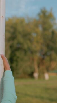 caucasian woman holding metal pole for balance drill in park, mint hoodie and tracksuit, focused expression and controlled lean, green grass and trees backdrop, mobility training for mature adult