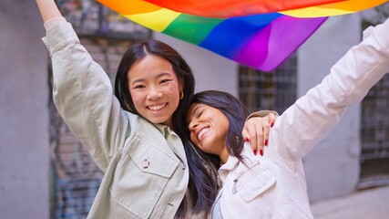 Smiling diverse women celebrating inclusion holding rainbow flag