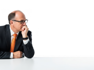 Businessman in suit and tie sitting at a table looking thoughtful isolated on white background