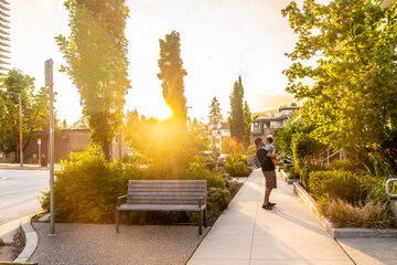 Fototapeta premium Father holding his baby while walking in a vancouver city park at sunset