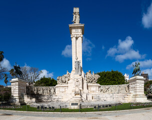 Obraz premium Cadiz, Spain - April 16, 2025: monument in homage to the Constitution of 1812 in Cadiz, with tourists swimming in the sea during the Easter holidays in Cadiz, Spain.