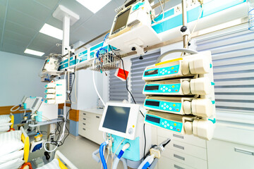 Medical equipment lines the walls of a hospital room. Monitors and machines are set up for patient care. The room is clean and organized for medical procedures
