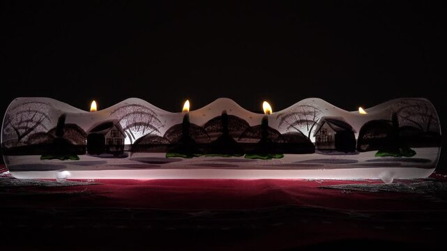 Eine leutende Glasleiste mit vier brennenden Teelichtern auf rotem Weihnachtstischtuch vor dunklem Hintergrund