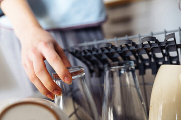 young woman putting dirty dishes into dishwasher at home