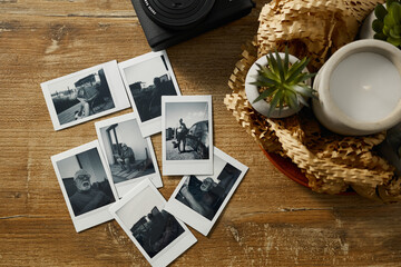 Group of black and white photos showing people and moments on a wooden table with a camera and plant nearby