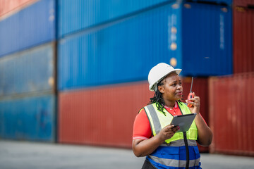 Confident supply chain professional coordinating container operations using walkie talkie communication and digital tablet technology.
